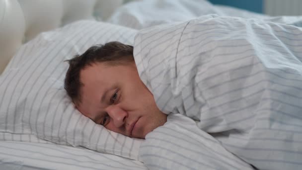 若い男は ベッドの毛布で覆われ 眠ることができない上に横たわる — ストック動画
