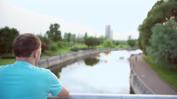 Молодий Чоловік Дивиться Річку Стоїть Парку Мосту Вид Ззаду Рух — стокове відео