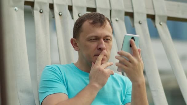 公園のベンチに座っている携帯電話を持つ魅力的な男 カメラの動き クローズアップ — ストック動画