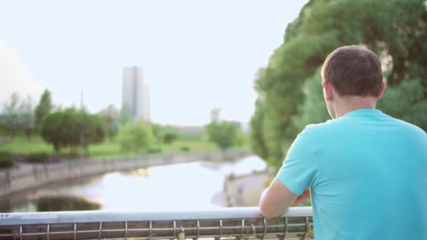 Young Man Stands Park Bridge Looks River Camera Movement Rear — Stock Video