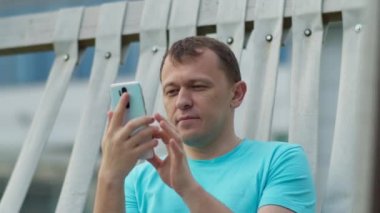 Parktaki bankta oturan cep telefonu olan bir adam, kamera hareketi.