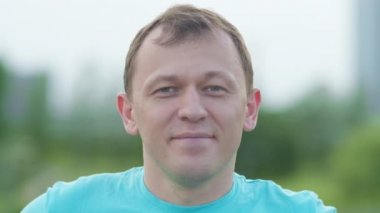 Gülümseyen bir adam parkta duruyor ve kameraya öpücük yolluyor.