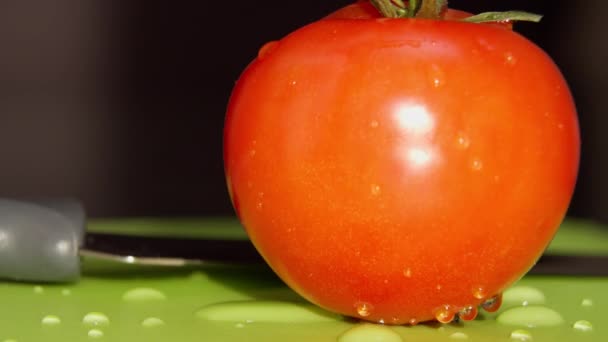 Une tomate juteuse mûre avec des gouttes d'eau est couchée sur une planche verte, gros plan — Video