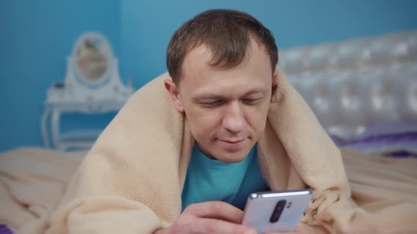 Egy Fiatalember Fekszik Hálószobájában Ágyon Egy Mobiltelefonnal — Stock videók