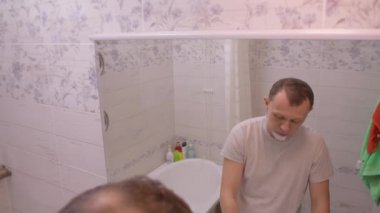 Sabah genç bir adam banyoda dikiliyor aynanın yanında tıraş oluyor, kamera hareket ediyor.
