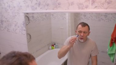 Sabah banyoda dikilen adam aynanın yanında tıraş oluyor, kamera hareket ediyor.
