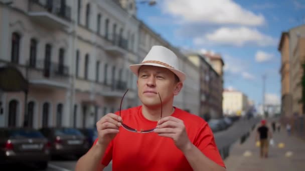 帽子を被った若者が街を歩きサングラスをかけカメラの動きをする — ストック動画