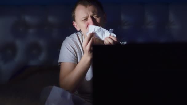 Young upset man crying, watching the news in the evening sitting at the TV, camera movement — Stock Video