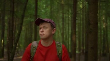 Şapkalı ve sırt çantalı bir gezgin karanlık ormanda yürür, kameraya doğru ilerler.