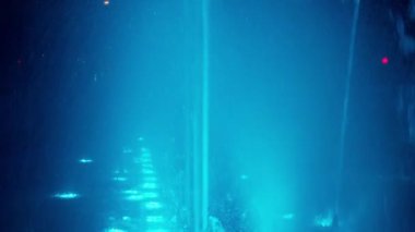 Gece bir sokak çeşmesinin renkli yansımaları, şehir ışıklarının arka planında, kamera hareketleri