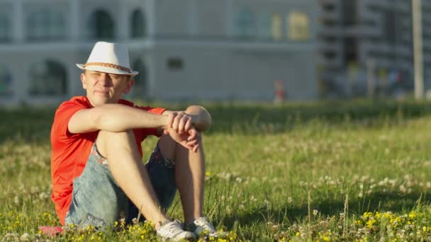Een Man Met Een Witte Hoed Zit Het Gras Een — Stockvideo