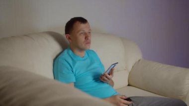 Adam akşamları kanepede oturur telefonda mesajlar okur ve TV 'de haberleri izler.