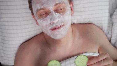 Yüzünde kozmetik kremle uzanan bir adam gözlerinin önünde salatalık dilimleri, üst manzara, kamera hareketleri...