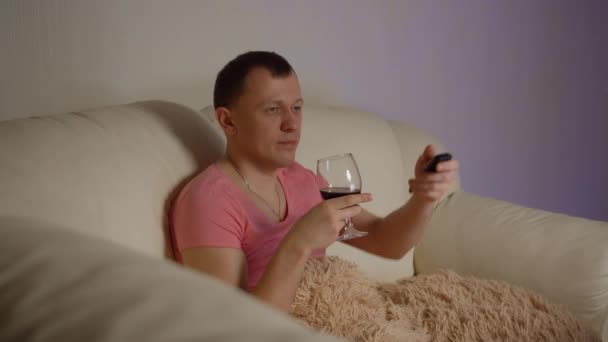 Junger Mann Kosmetikmaske Trinkt Rotwein Und Sieht Abends Fern Sitzt — Stockvideo