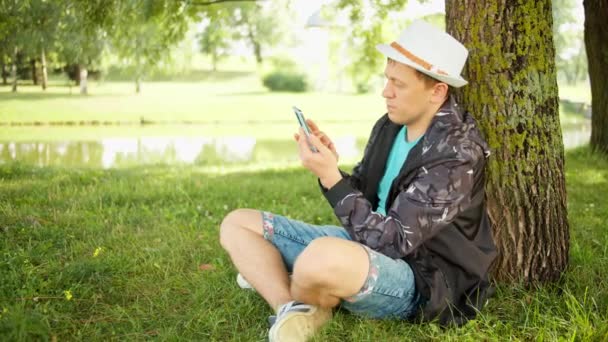 Elinde Telefon Olan Bir Adam Parkta Bir Ağacın Altında Oturuyor — Stok video