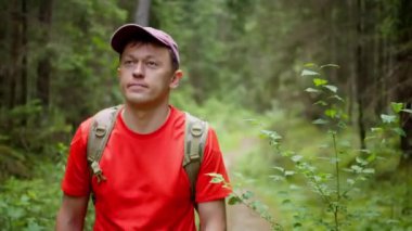 Sırt çantalı ve şapkalı gezgin orman yolunda yürüyor, kamera takibi yapıyor.