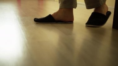 Terlikli bir adam aydınlık zeminde yürür, kamera takibi yapar.