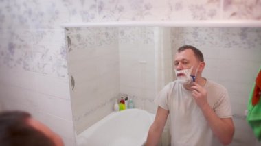 Genç çekici bir adam banyoda aynanın önünde dikiz aynasından tıraş oluyor.