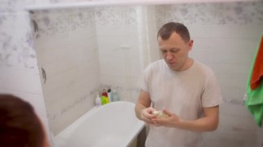 Genç çekici adam banyoda dururken parfüm kullanıyor.
