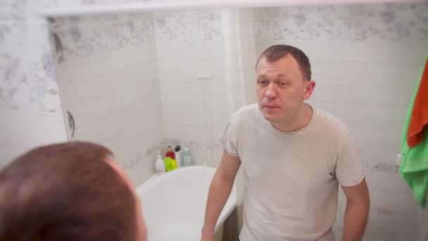 Jeune homme tombé malade, s'examine dans le miroir, vue arrière — Video