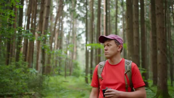 Молодой турист с рюкзаком ходит по лесу с фляжкой в руках, отслеживая камеру — стоковое видео
