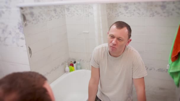 Genç adam banyoda dikilirken aynadaki yansımasını inceliyor. — Stok video
