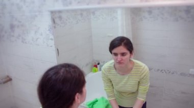 Kız sabah banyoda aynanın karşısında durup yüzünü havluyla silerken yüzünü yıkıyor.