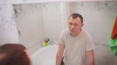 Genç adam kendine bakar ve dilini gösterir.