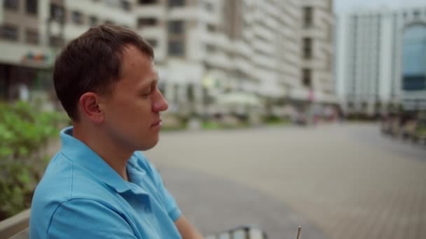 Портрет мужчины, сидящего на уличной скамейке, надевающего солнцезащитные очки, движения камеры — стоковое видео