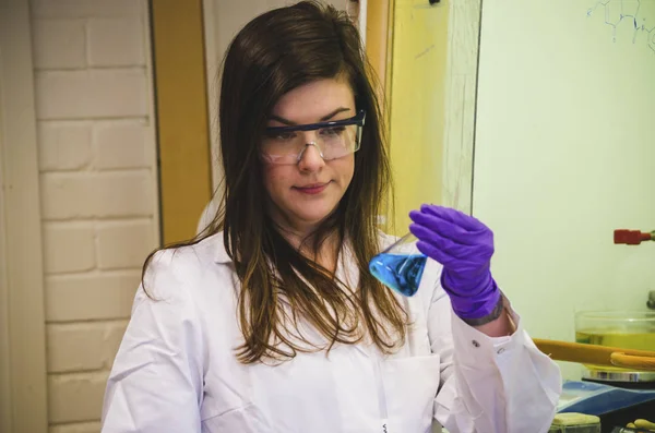 Beautiful woman scientist holding and investigating a blue solut