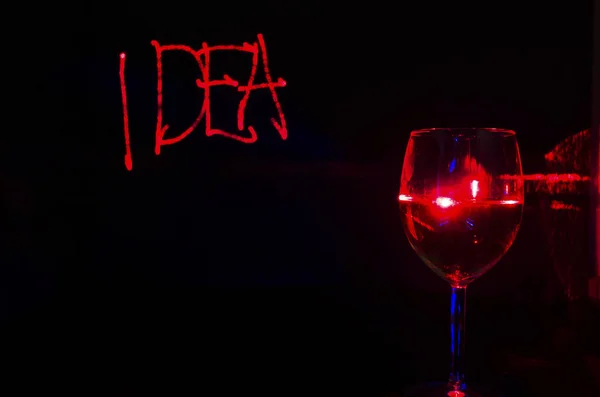 Red Laser drawn idea writing in a black background with wine gla