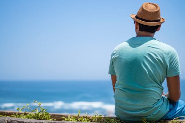 Bir turist, Endonezya, Bali 'de bir sahil kenarında, renkli elbiseler ve yuvarlak şapkalar giyip, sıcak yaz güneşinin tadını çıkarıyor.