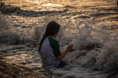 Yerel bir çocuk gün batımında Endonezya, Bali 'de deniz dalgalarıyla oynuyor.
