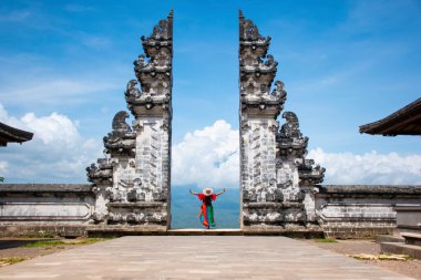 Hindu tapınağının kapısında fotoğraf çeken yalnız bir turist. Endonezya, Bali 'de mavi arka planda gökyüzü olan renkli bir Sarong giyiyor.