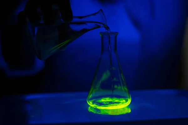 ダーク生化学研究室のガラス円錐フラスコ中の緑色蛍光化合物を用いた医療開発のための化学者 — ストック写真