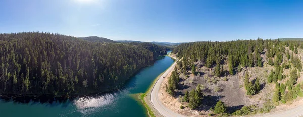 Bir gölün yanında dolambaçlı bir yol boyunca giden kırmızı arabanın havadan panorama görüntüsü