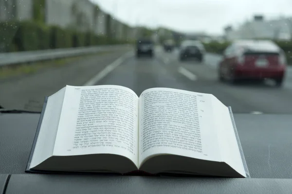Open Hebrew Holy Bible on a rainy day. Blurred background with expressway and cars. — Stock Photo, Image