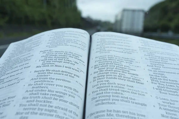 在诗篇91的开放圣经特写。带雨滴的挡风玻璃。高速公路和汽车的模糊背景. — 图库照片