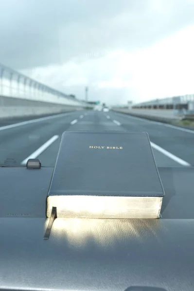 Closed Bible with golden glow. Blurred background expressway with cars.