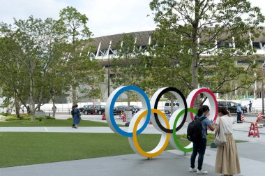 SHINJUKU CITY, TOKYO, JAPAN - SEPTEMBER 30, 2019: Japanese tourists taking picture of Olympic Rings, pedestrians and working men. Background with New National Stadium (Tokyo). clipart