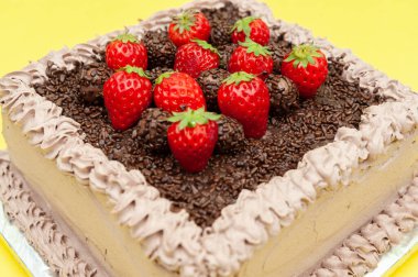 Lezzetli geleneksel Brezilya çikolatalı keki Bolo de Brigadeiro taze çilek soslu. Sarı arka planda izole edilmiş. Yakın plan. Üst görünüm.