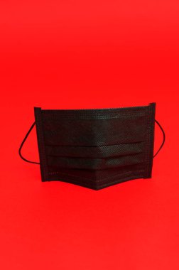 Coronavirus (COVID-19) ve diğer bulaşıcı hastalıklara karşı korunmak için siyah cerrahi maske. Uzayı kopyala Dikey çekim. Kırmızı arkaplanda izole.