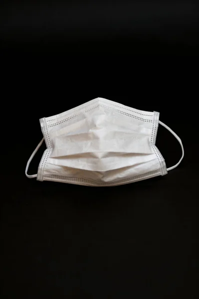 Health care - White surgical mask for protection against Coronavirus (COVID-19) and other infectious diseases. Isolated on black background. Copy space. Vertical shot.