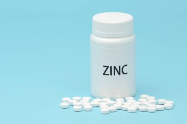 ZINC beyaz şişe ambalajında dağınık haplarla. Besin takviyesi. COVID-19 tedavisi. Mavi arka planda izole edilmiş. Yatay çekim. Boşluğu kopyala.
