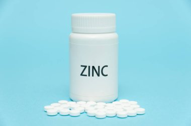 ZINC beyaz şişe ambalajında dağınık haplarla. Besin takviyesi. COVID-19 tedavisi. Mavi arka planda izole edilmiş. Yakın plan. Uzayı kopyala Yatay çekim.