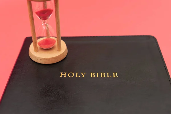 Holy Bible, the Word of God with hourglass. Isolated on red background. Top view. Horizontal shot.