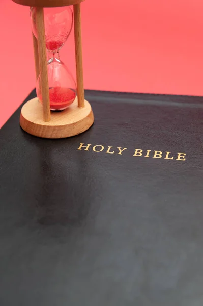 Holy Bible, the Word of God with hourglass. Isolated on red background. Top view. Close-up. Copy space. Vertical shot.
