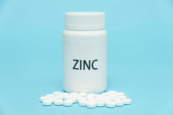 ZINC beyaz şişe ambalajında dağınık haplarla. Besin takviyesi. COVID-19 tedavisi. Mavi arka planda izole edilmiş. Yakın plan. Uzayı kopyala Yatay çekim.
