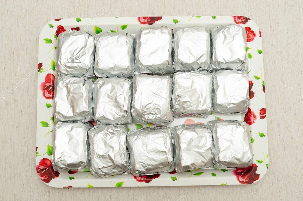 Traditional Brazilian dessert known as BOLO GELADO in Portuguese - Making step by step: cakes wrapped in aluminum foil placed on tray. Top view. Isolated on white background. Horizontal shot.