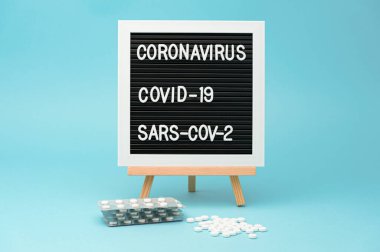 İlaç paketleri ve dağınık haplarla yazı tahtası. COVID-19 tedavisi. Mavi arka planda izole edilmiş. Yatay çekim.